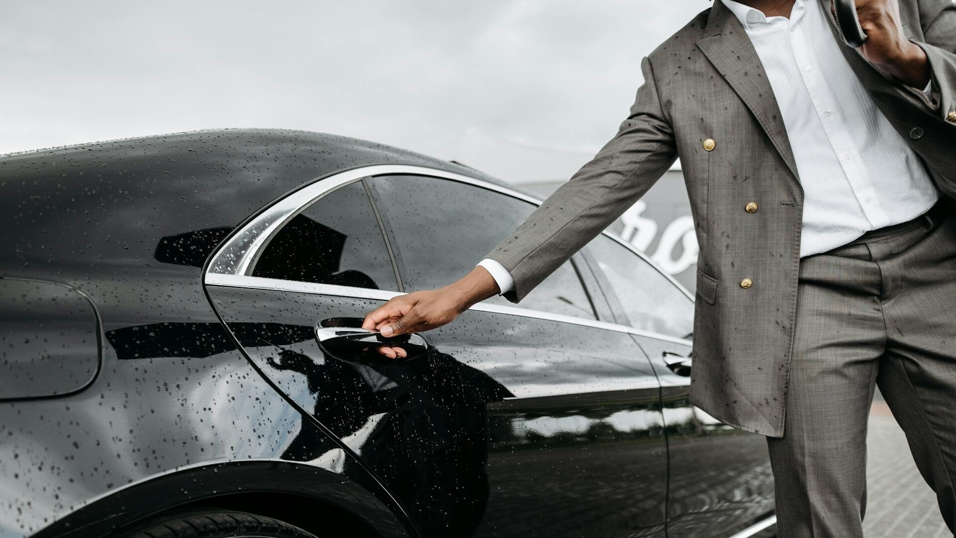 Chauffeur in a dark suit holding the rear door of a black executive sedan open for a business passenger in Los Angeles